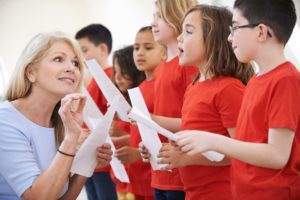 Children In Singing Group Being Encouraged By Teacher