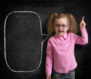 Funny child in eyeglasses standing near school chalkboard  as a